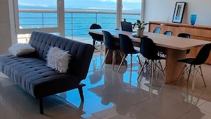 Ein modernes Wohnzimmer mit einer Couch, einem Esstisch, Stühlen und Blick auf den Ozean.