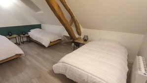 Een kamer met drie bedden, houten hoofdborden en een schuine balkenkap.