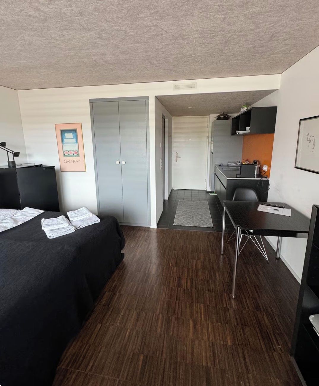 Ein Hotelzimmer mit Bett, Schreibtisch, Stuhl, einer Küchenzeile und einer Tür zu einem weiteren Raum.