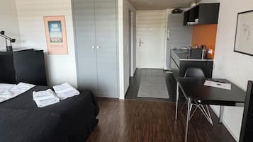 Ein Hotelzimmer mit Bett, Schreibtisch, Stuhl, einer Küchenzeile und einer Tür zu einem weiteren Raum.