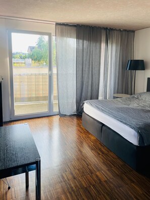 Ein Schlafzimmer mit Bett, Schreibtisch, Lampe und Blick durch eine Schiebetür.