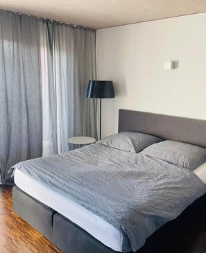 A modern bedroom with a bed, a bedside table, a lamp, and a window with curtains.