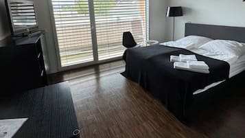 Ein Hotelzimmer mit einem Bett, einem Schreibtisch, einem Sessel, einem Fernseher und einem Fenster mit Jalousien.