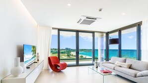 A modern living room with a large TV, a red chair, a sofa, and a glass coffee table. - 602- Stunning one bedroom oceanview (Cupecoy)