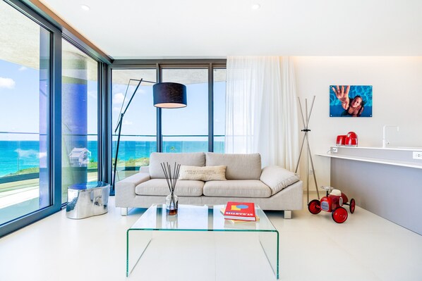 A modern living room with a glass coffee table, a sofa, and a view of the ocean.