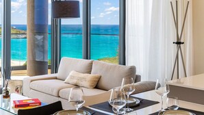 A modern dining area with a view of the ocean, a sofa, and a table set for four. - 602- Stunning one bedroom oceanview (Cupecoy)