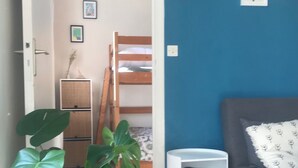 A room with a bunk bed, a small white side table, a grey sofa, and a large green plant.