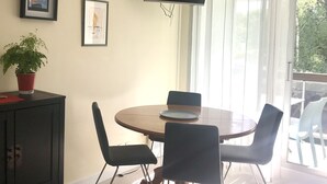 A dining area with a round table, four chairs, a television mounted on the wall, and a potted plant on a cabinet.