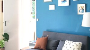A room with a blue wall, a grey sofa with cushions, a hanging light fixture, and framed artwork.