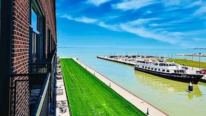 Ein Fluss mit einem am rechten Ufer vertäuten Boot, einem grasbewachsenen Uferweg und einem Gebäude mit Ziegelverkleidung links.