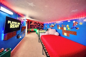 A room with a Nintendo-themed wall, a bed, a TV, and a gaming console.