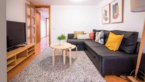Una sala de estar moderna con un sofá de cuero negro, un mueble de televisión de madera, una mesita redonda con una planta y una alfombra con textura.