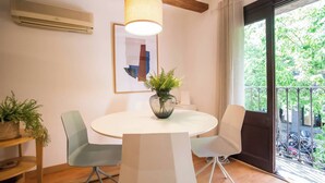 Un comedor con una mesa redonda, dos sillas, un jarrón con planta, un ventilador de techo y una ventana con vista a follaje.