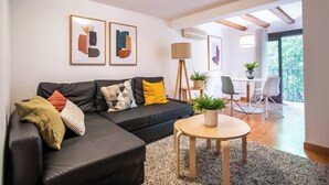 Una sala de estar moderna con un sofá de cuero negro, una mesa de centro redonda de madera y un comedor con mesa y sillas blancas.