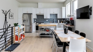 A modern kitchen with white cabinets, a stainless steel refrigerator, a wooden dining table with chairs, and a TV mounted on the wall. - Downtown Ballard View Home Walk to Bars & Shops (Seattle)