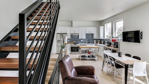A modern kitchen with white cabinets, a central island, and a dining area with a table and chairs. - Downtown Ballard View Home Walk to Bars & Shops (Seattle)