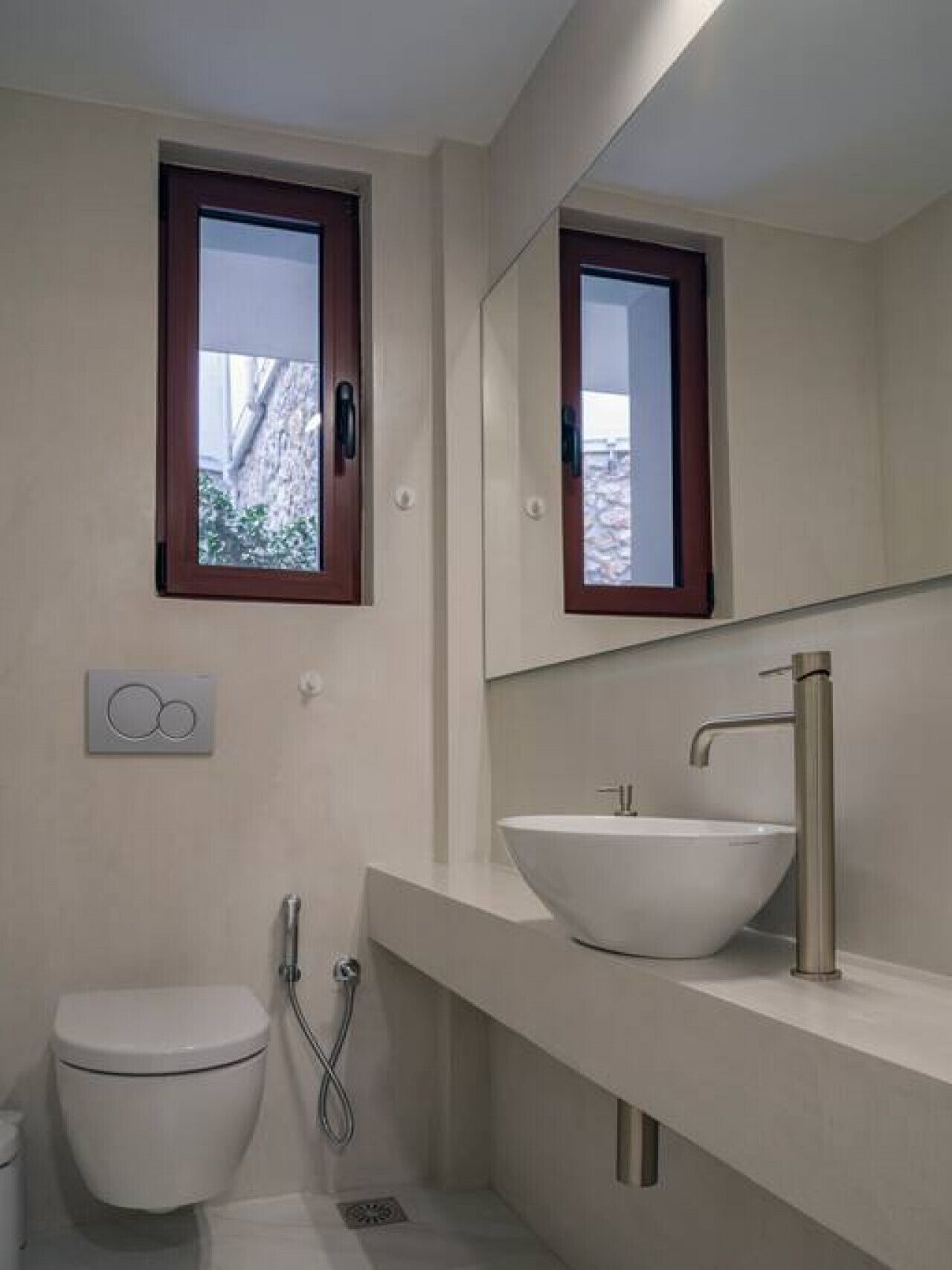 Une salle de bain moderne équipée de toilettes, d’un bidet et d’un grand miroir au-dessus d’un lavabo avec un receveur apparent.