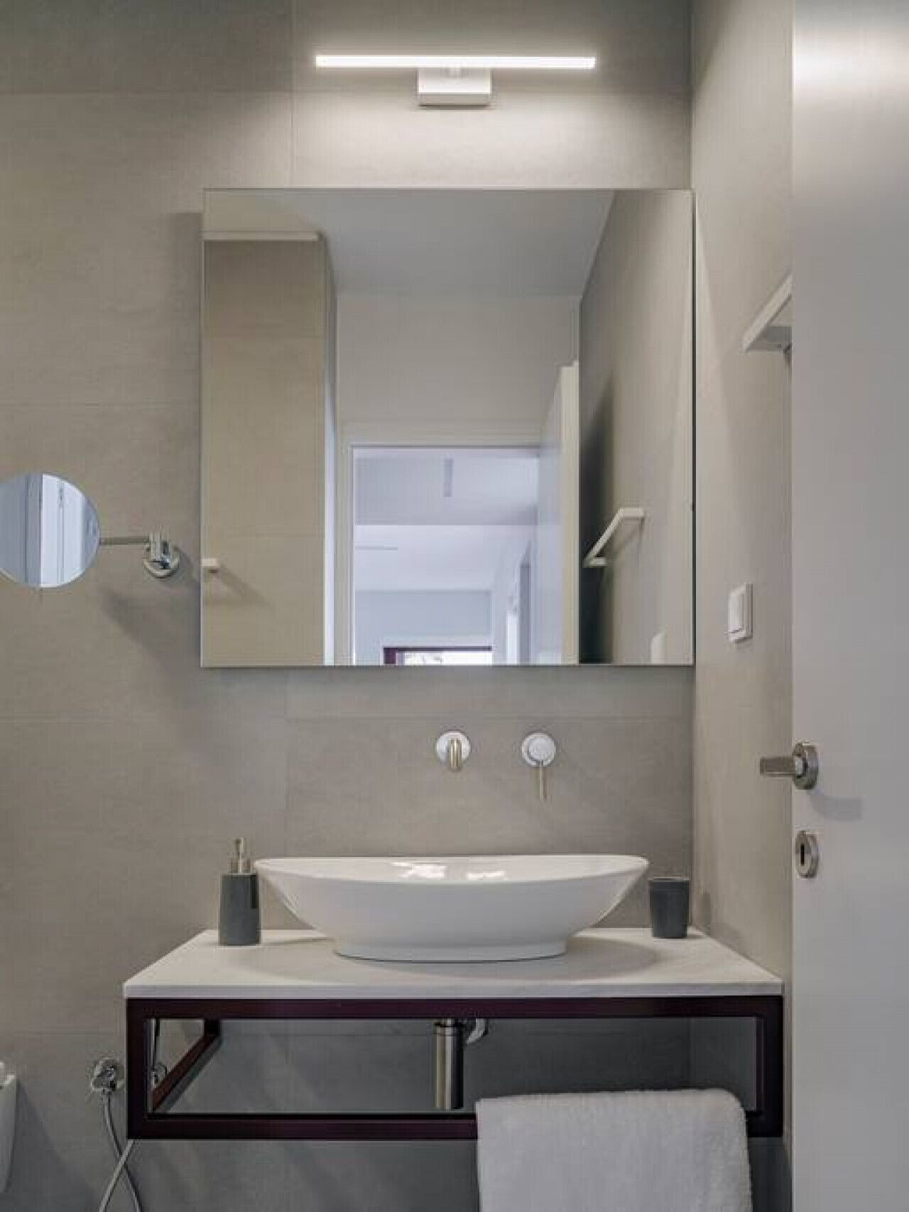 A modern bathroom with a large mirror, a vessel sink, and a towel hanging on the wall.