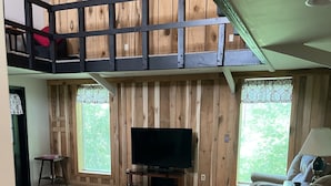 A cozy living room with a TV, a sofa, a chair, and a table. There's a wooden wall and a window with a view. - Beautiful loft cabin!  (Baxter)