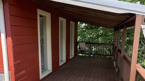 A wooden deck with a covered porch, white window shutters, and a view of trees. - Beautiful loft cabin!  (Baxter)
