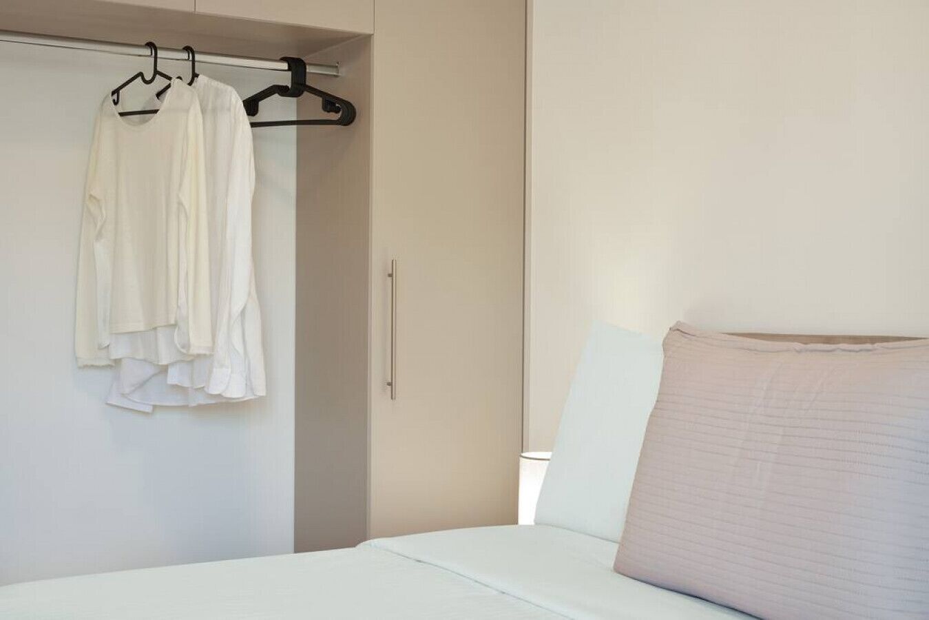 A bedroom with a bed, a hanging closet with clothes, and a door.