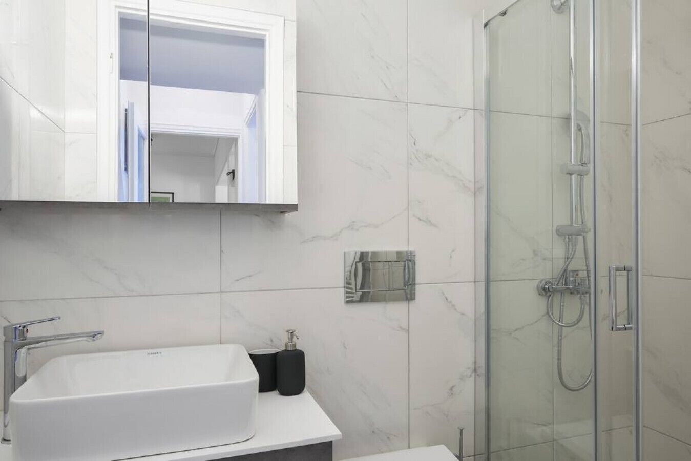 Une salle de bain avec un lavabo blanc, un miroir et une cabine de douche en verre.