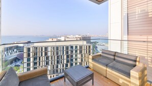 Ein Balkon mit Korbmöbeln, einer Glasreling und Blick auf Stadt und Wasser.