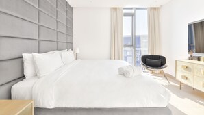 Ein modernes Hotelzimmer mit einem großen Bett, einem Flachbildfernseher, einem Sessel und einer Kommode.