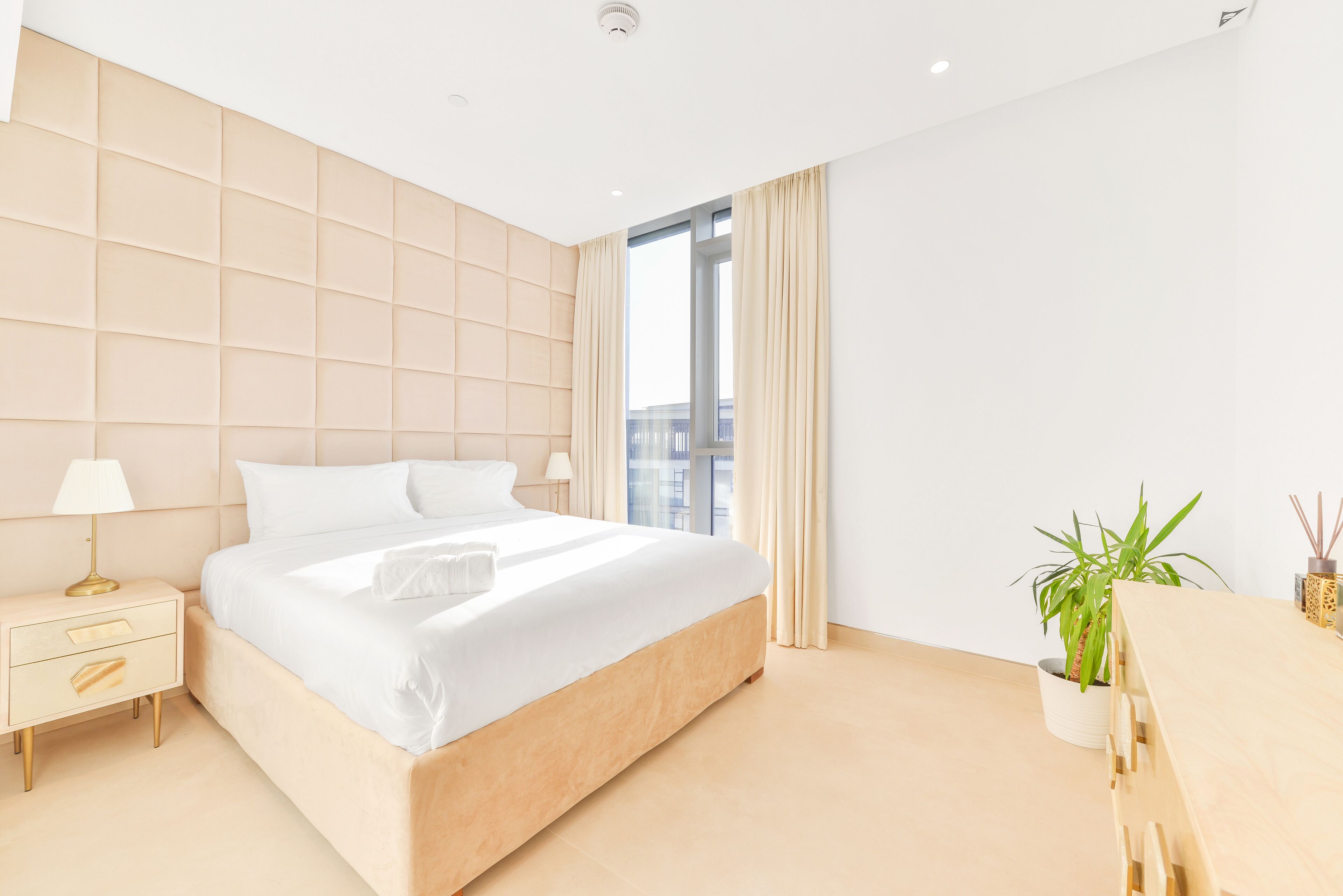 Ein modernes Hotelzimmer mit einem großen Bett, Nachttischen, einem Schreibtisch und einer Zimmerpflanze.