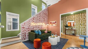 Een moderne woonkamer met een groene bank, een trap met behang met patroon, en een bordje met de tekst 'Late Night Music'.