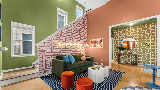 Een moderne woonkamer met een groene bank, een trap met behang met patroon, en een bordje met de tekst 'Late Night Music'.