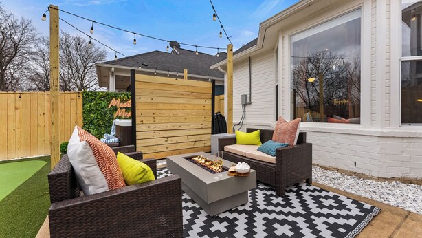 Een terras buiten met rieten meubilair, een vuurkorf en een patroonrijk vloerkleed.