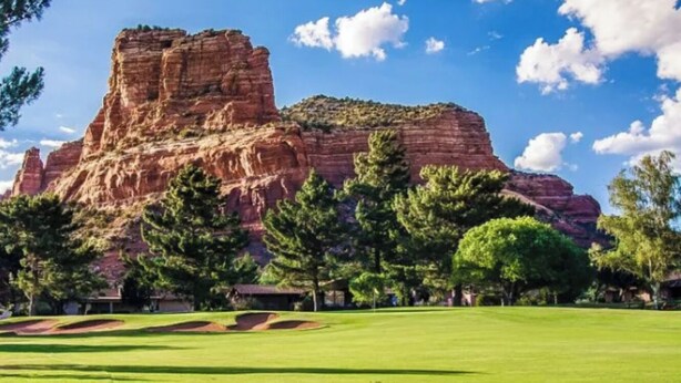 A golf course with a prominent red rock formation in the background.