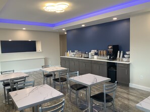 A modern kitchen with marble countertops, a built-in coffee station, and a seating area with metal chairs and tables. - Days Inn by Wyndham Troy IL (Troy)