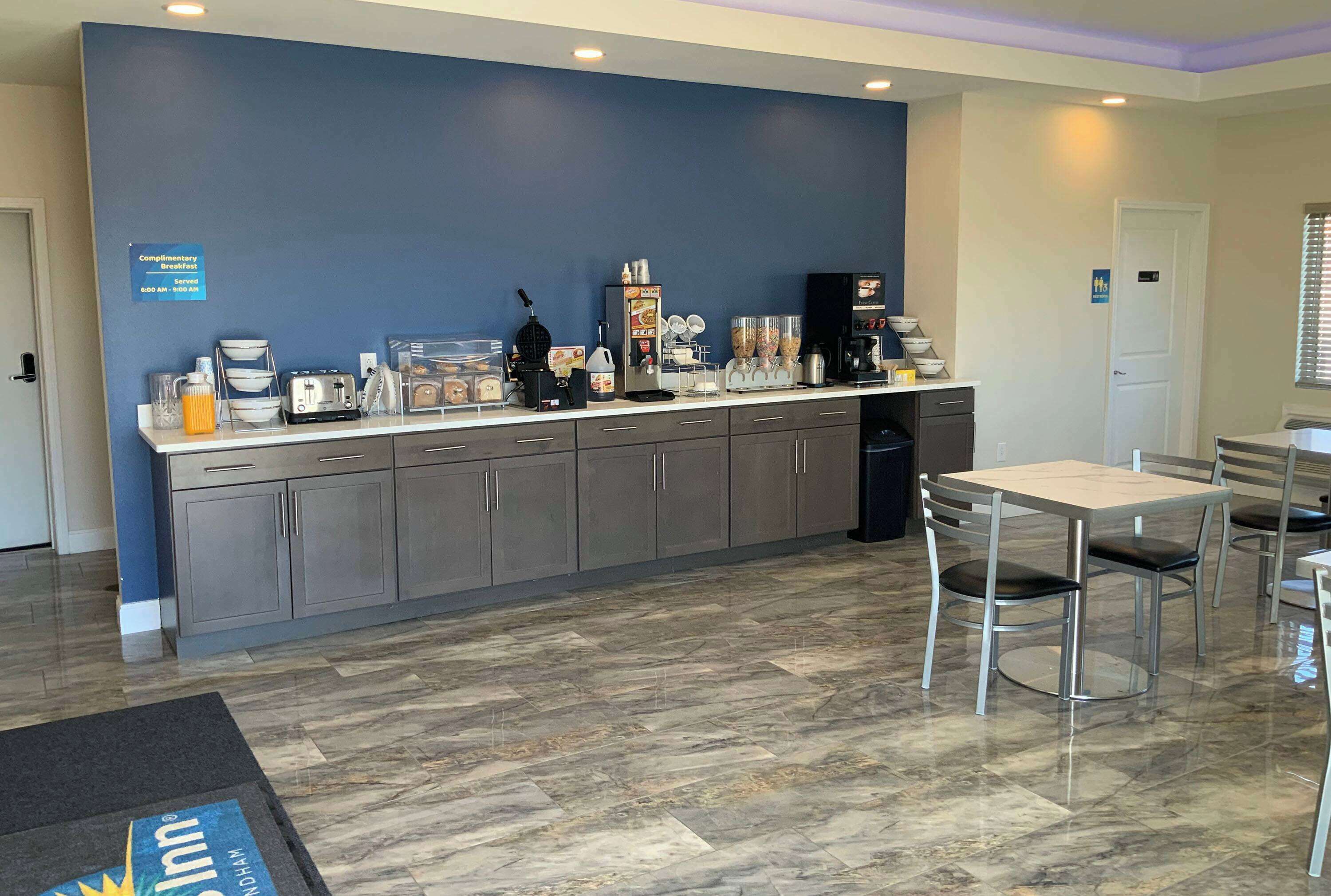 Et hotelkøkken med morgenmadsbar, kaffemaskiner og et skilt, der angiver tidspunkter for gratis morgenmad.