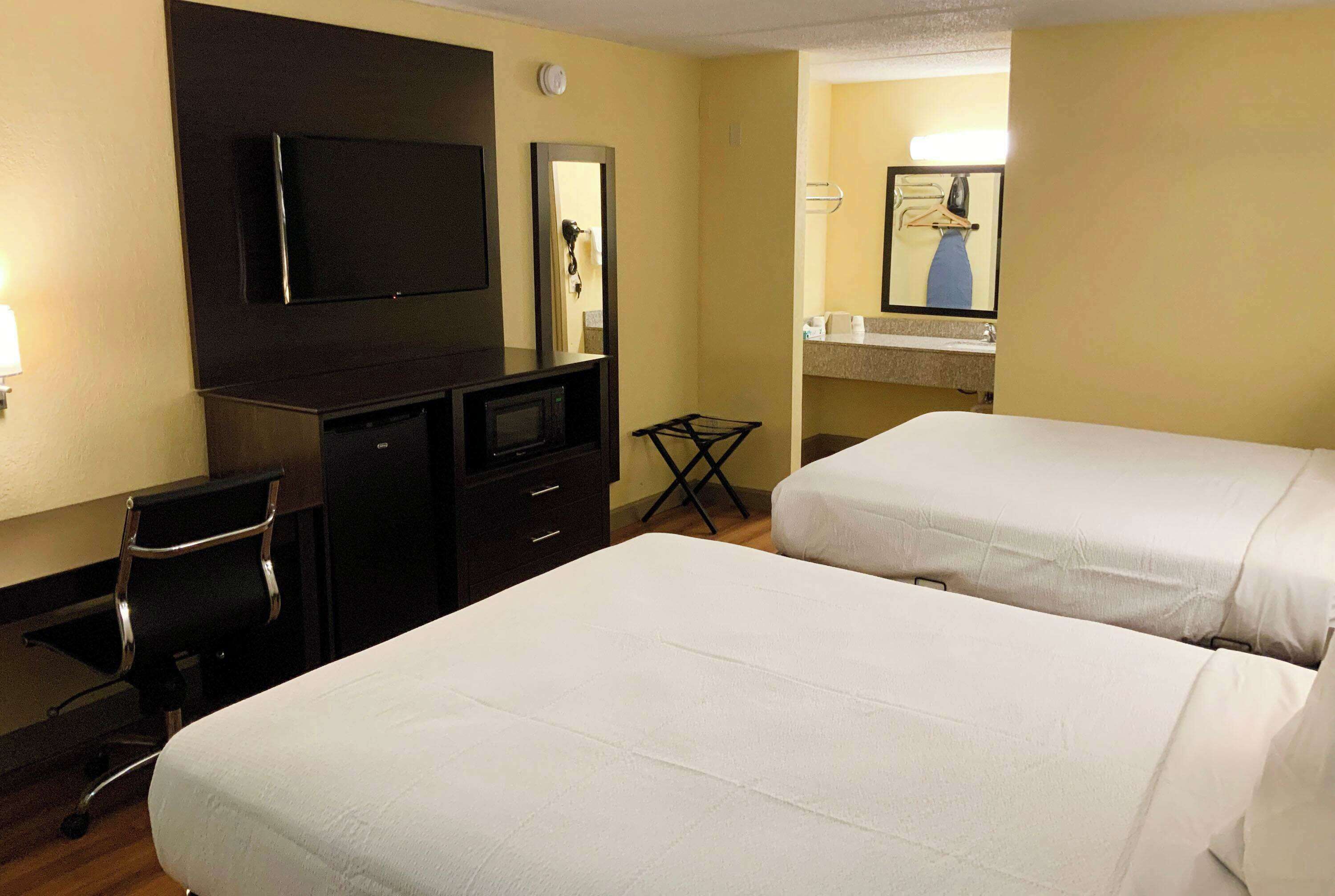 Ein Hotelzimmer mit zwei Betten, einem Schreibtisch mit Fernseher, einem Spiegel und einer kleinen Sitzecke.