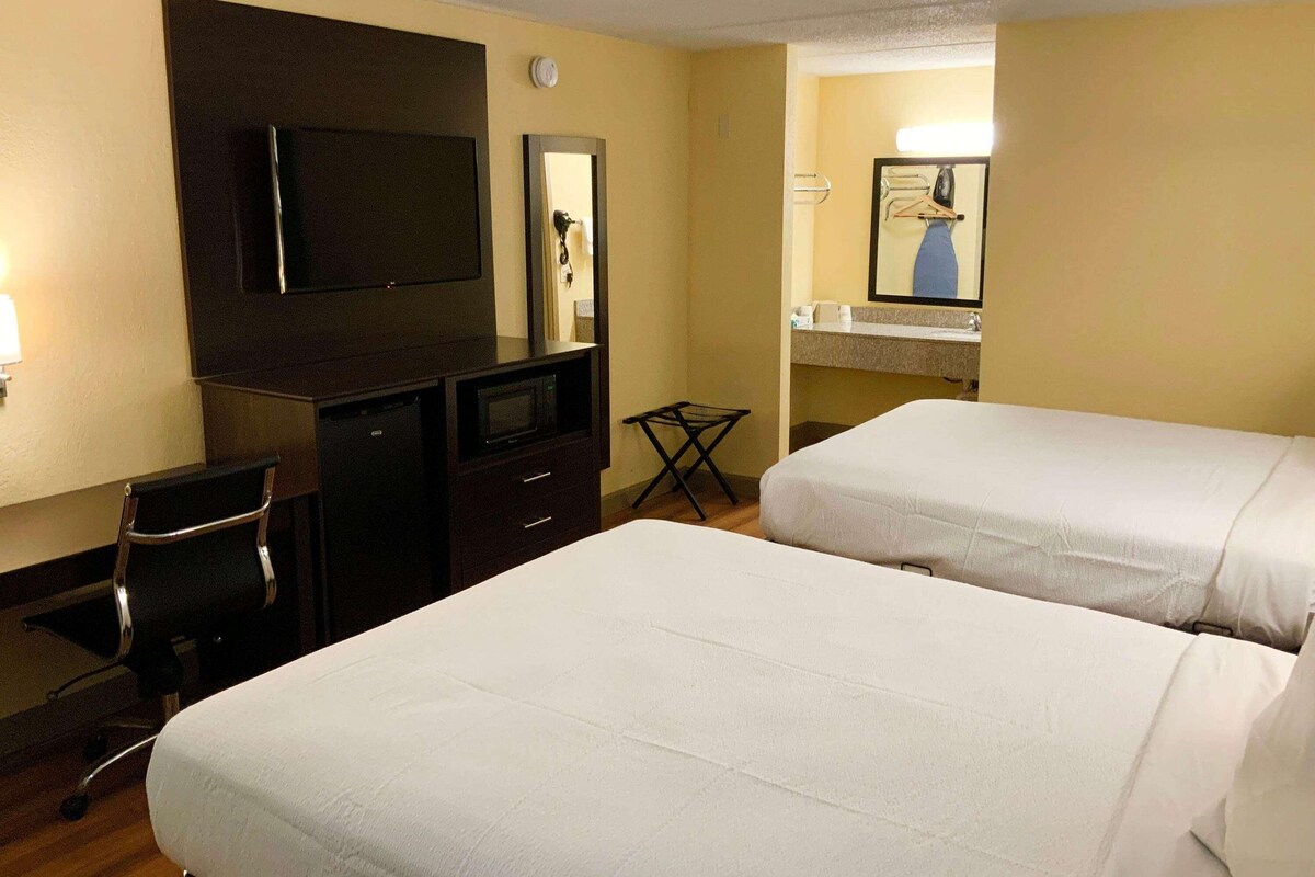A hotel room with two beds, a desk with a TV, a chair, and a small table.