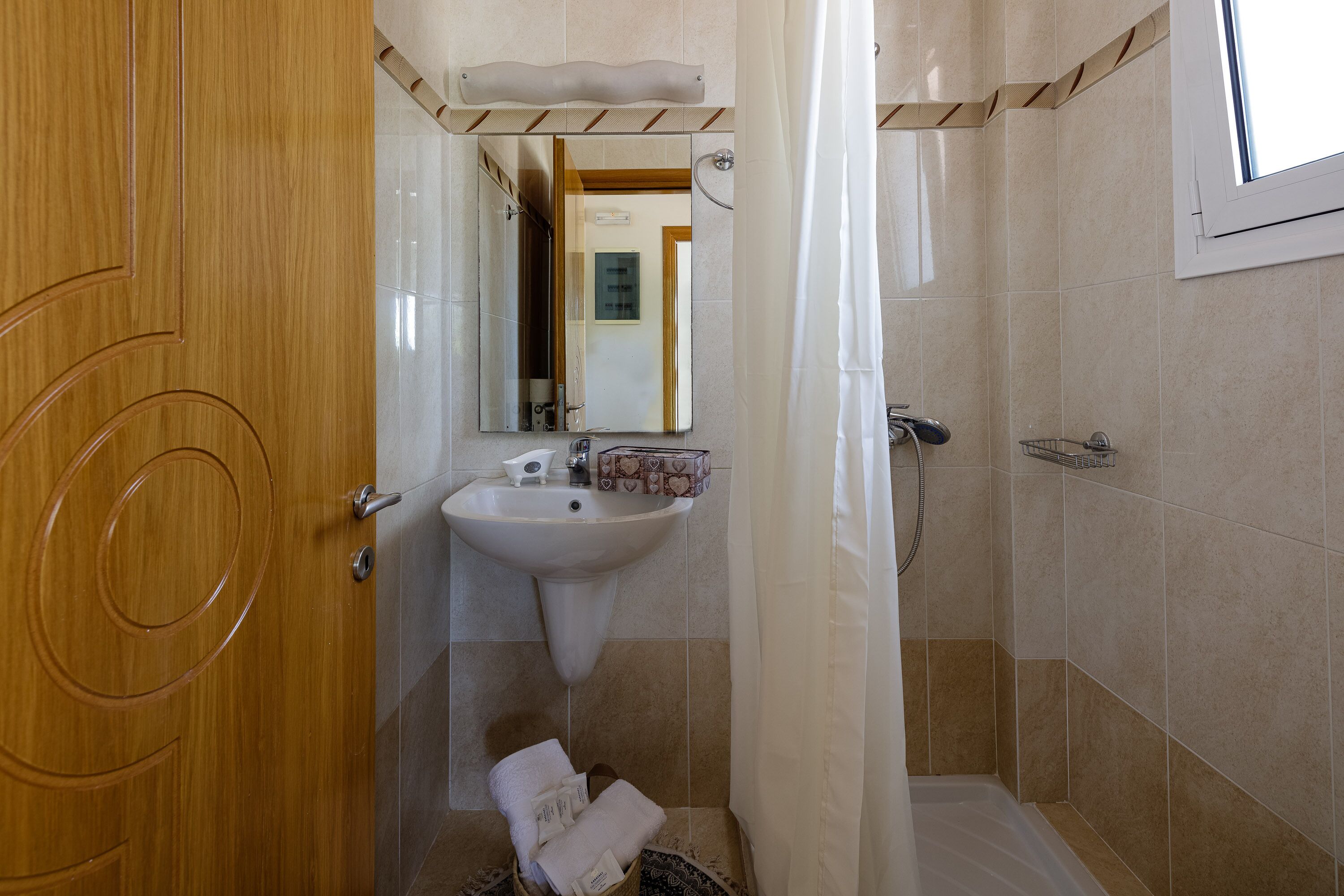 A bathroom with a wooden door, a sink, a shower, and a window.