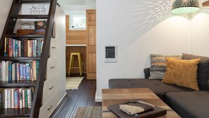 Een gezellige woonkamer met een boekenkast, een houten trap, een bank met kussens en een hanglamp.