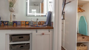 Een badkamer met een houten aanrecht, een wastafel, een spiegel en een plank met manden.