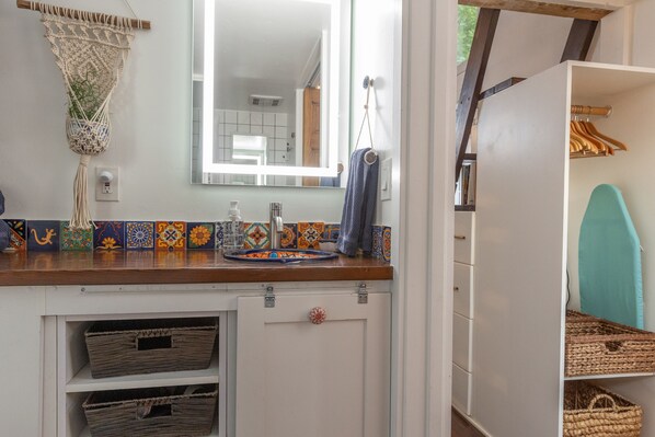A bathroom with a wooden countertop, a sink, a mirror, and a shelf with baskets.