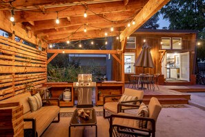 An outdoor patio with wooden furniture, string lights, and a grill.
