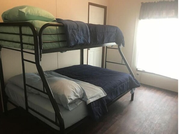 A bunk bed with two levels, a window with a curtain, and a door in the background.