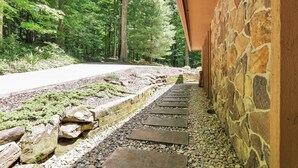 A stone pathway leading to a building with a stone exterior wall, surrounded by a forested area. - Salt Run Retreat| Trails, Decks, & Screened Porch (Granville)