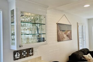 Een kamer met een glazen kast die divers glaswerk toont, een lijst met een afbeelding aan de muur, en nautische decoratie.