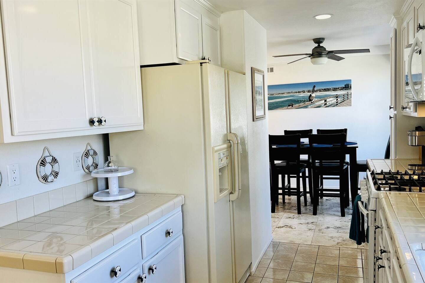 A kitchen with white cabinets, a refrigerator, a dining area with chairs, and a ceiling fan.