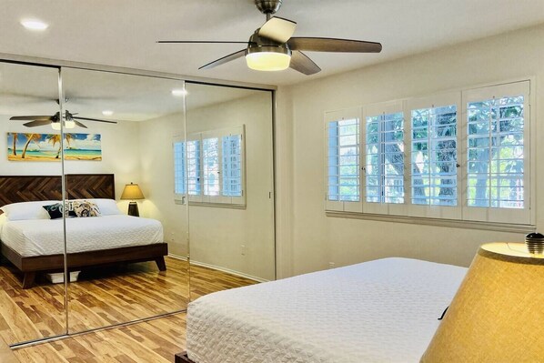 A bedroom with a bed, a ceiling fan, a nightstand, a lamp, and a window with blinds.