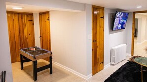 Une pièce avec une table de ping-pong, des portes en bois, un radiateur blanc et un téléviseur fixé au mur.