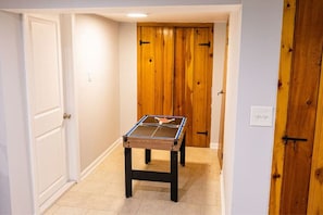 Un pasillo estrecho con una mesa de ping pong en el centro, puertas de madera a ambos lados y un interruptor de luz en la pared.