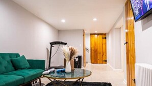 Un salon moderne avec un canapé vert, une table basse en verre et un téléviseur fixé au mur.